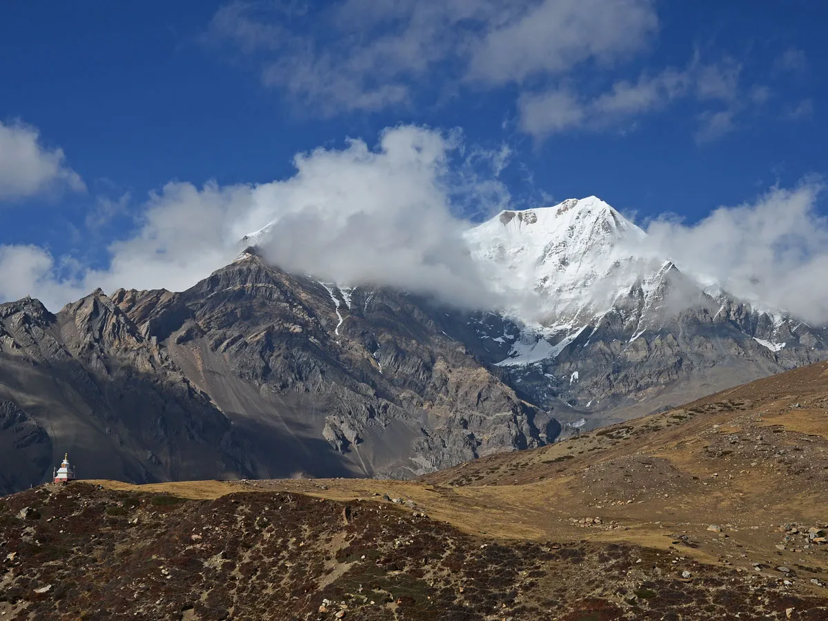 Snow-capped Annapurna peaks towering over dry terrain with a small Buddhist chorten in the foreground.