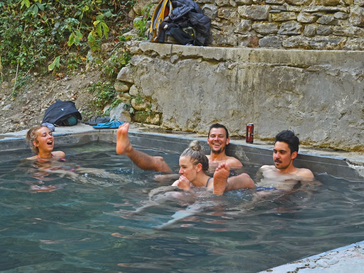 A group of tourists sitting, relaxing, and laughing in the outdoor natural hot spring pool at Jhinu Danda.