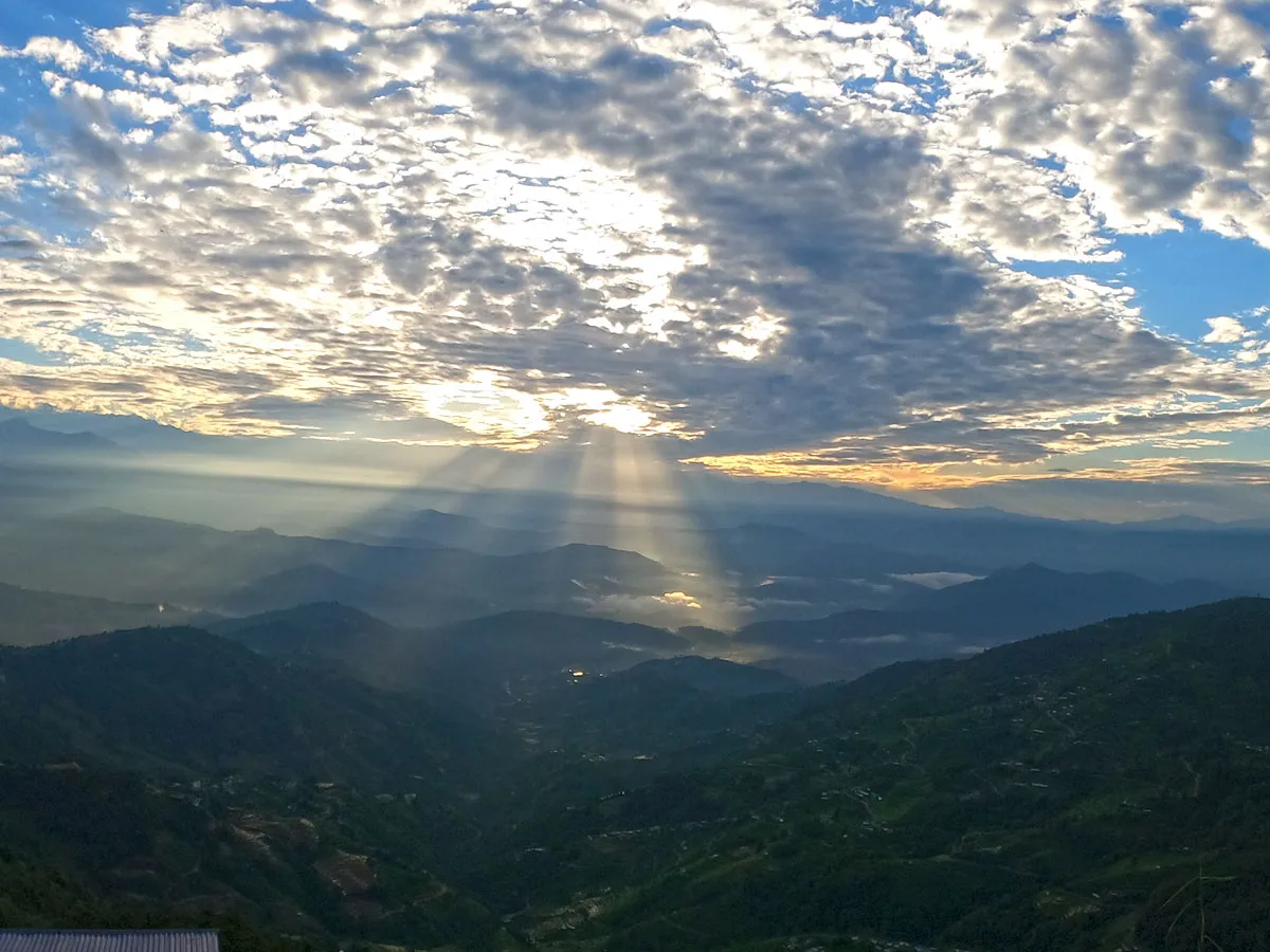 Sunlight rays bursting dramatically through cloudy sky onto mist-covered mountain valleys during sunrise along the Kathmandu Valley rim