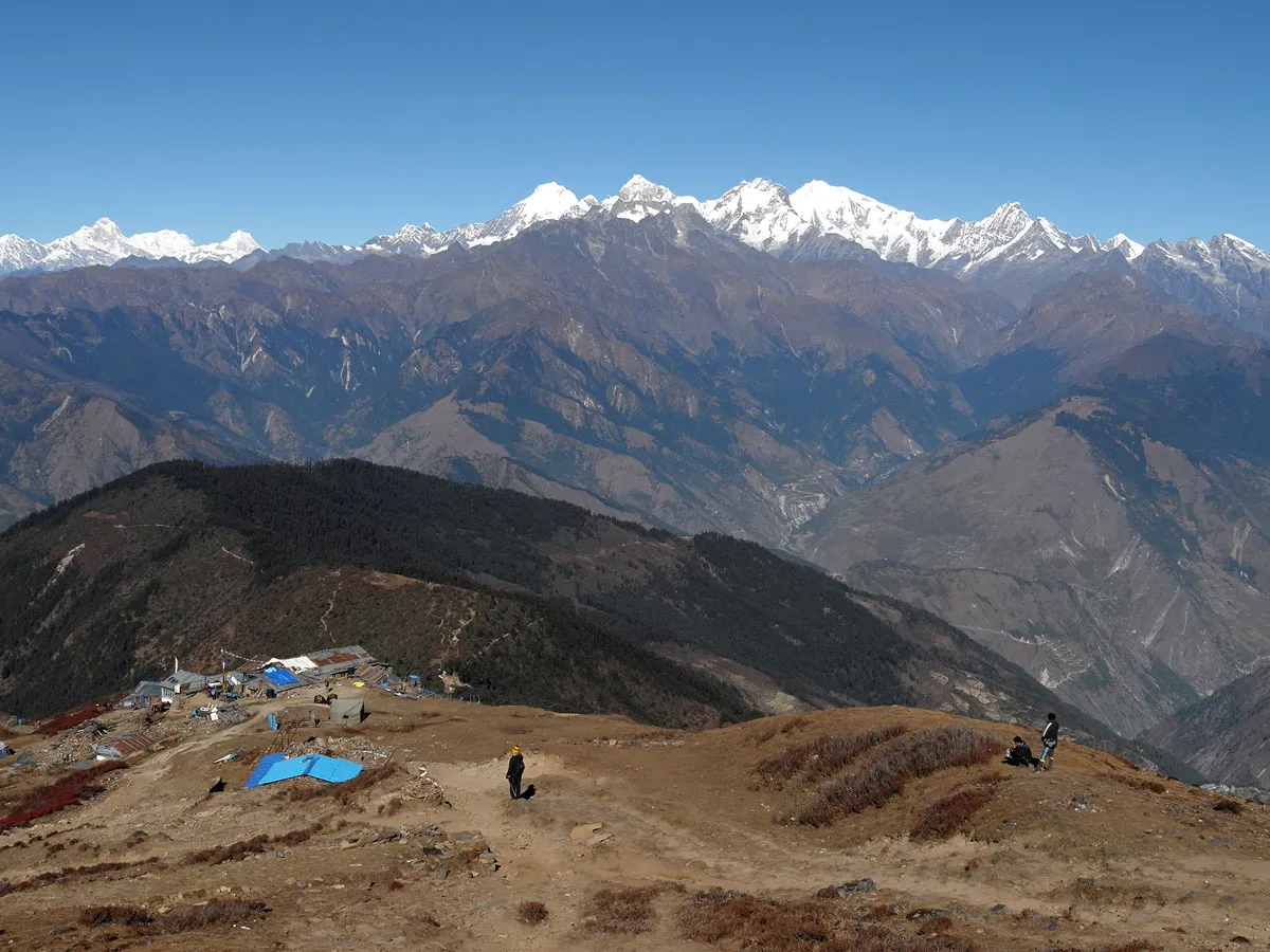 Trekkers walking along a high mountain ridge near Lauribina Pass with expansive views of deep valleys and snow-covered Himalayan peaks.