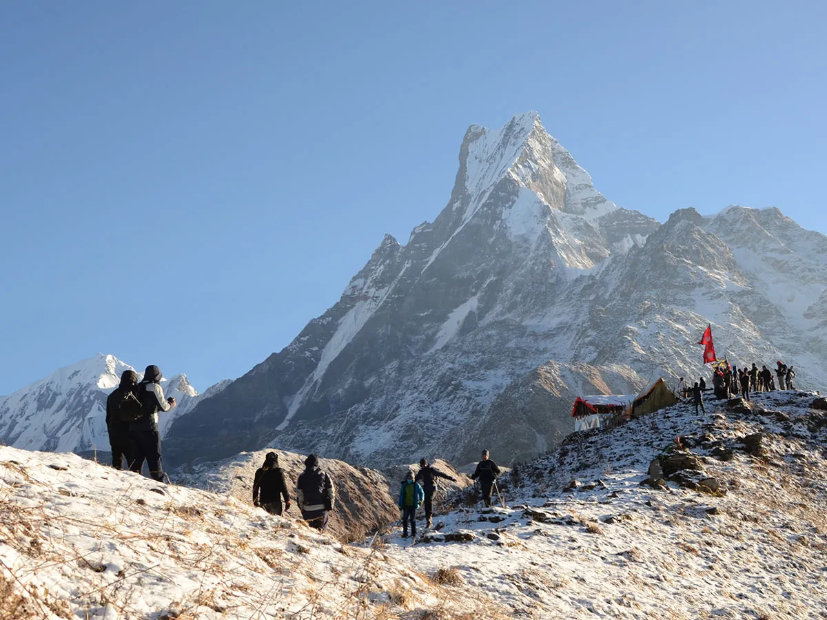 Hikers walking along a snowy ridge toward Mardi Himal Base Camp with Mt. Fishtail in the background