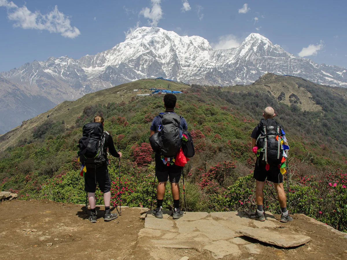 Three trekkers with backpacks taking in panoramic views of the snow-capped Annapurna mountain range