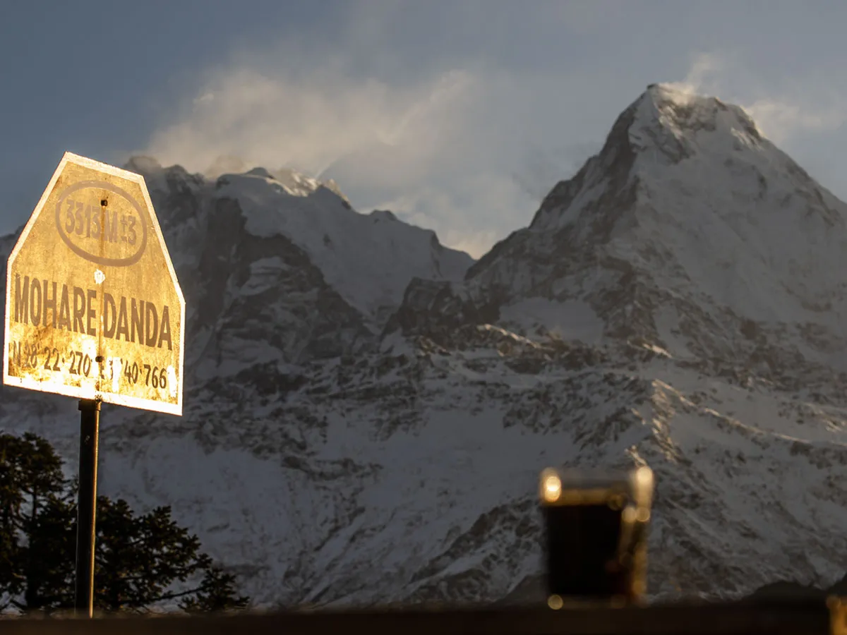 A signpost labeled Mohare Danda set against a dramatic backdrop of snow-capped Himalayan mountain peaks.