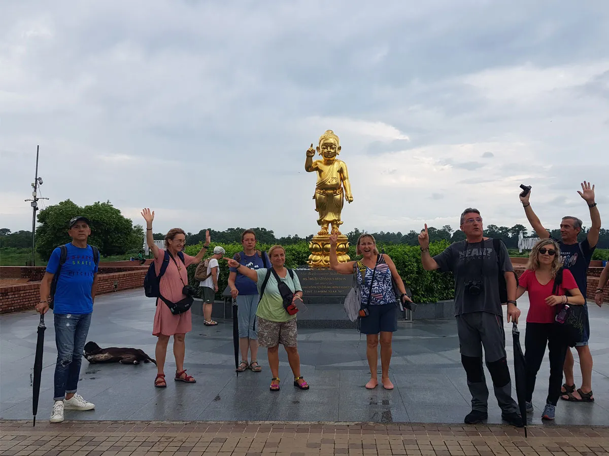 A group of international tourists standing together and raising their hands in front of the golden statue of the infant Buddha in Lumbini