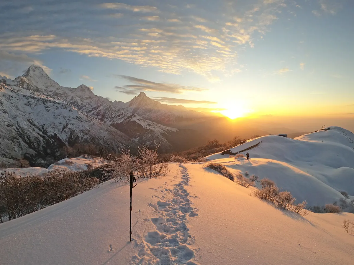 Golden sunrise casting light across a snow-covered trekking trail towards Annapurna and Machhapuchhre mountains on the Muldai Trek.