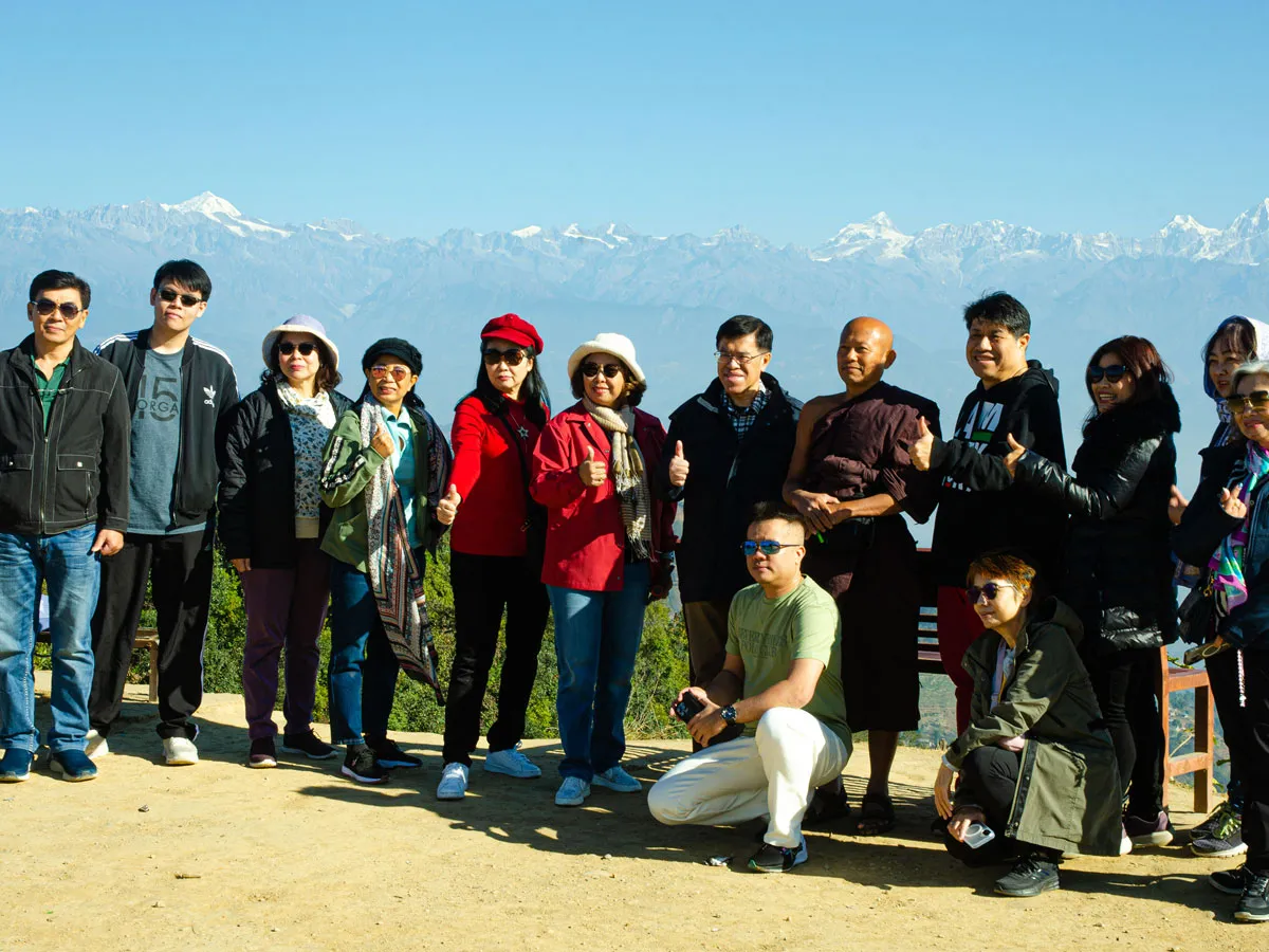 A tour group posing outdoors against a panoramic view of the snow-capped Himalayan mountain range