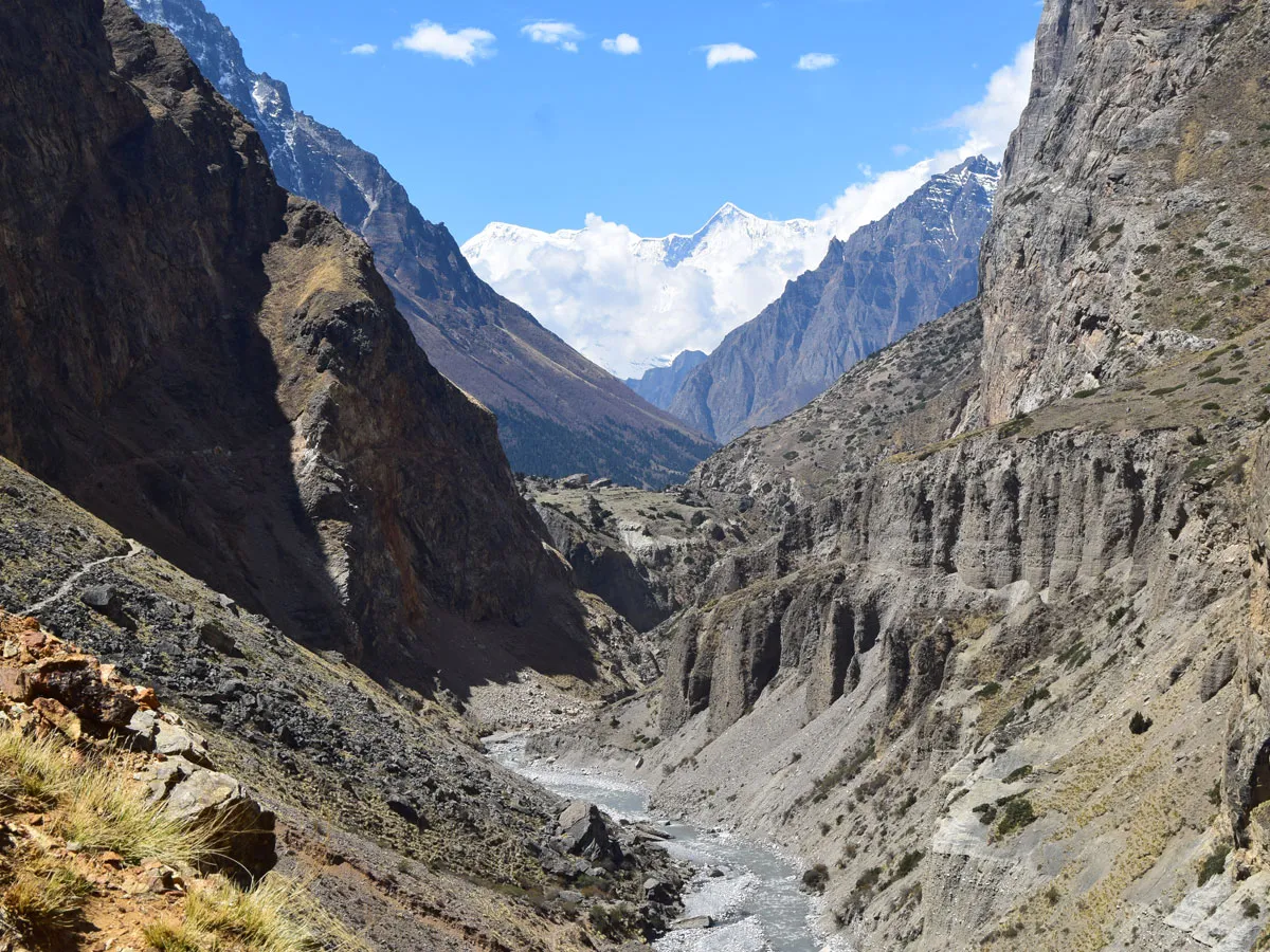 Deep rocky river gorge and canyon leading toward a distant snow-covered Himalayan peak under a clear blue sky in Nar Phu Valley.