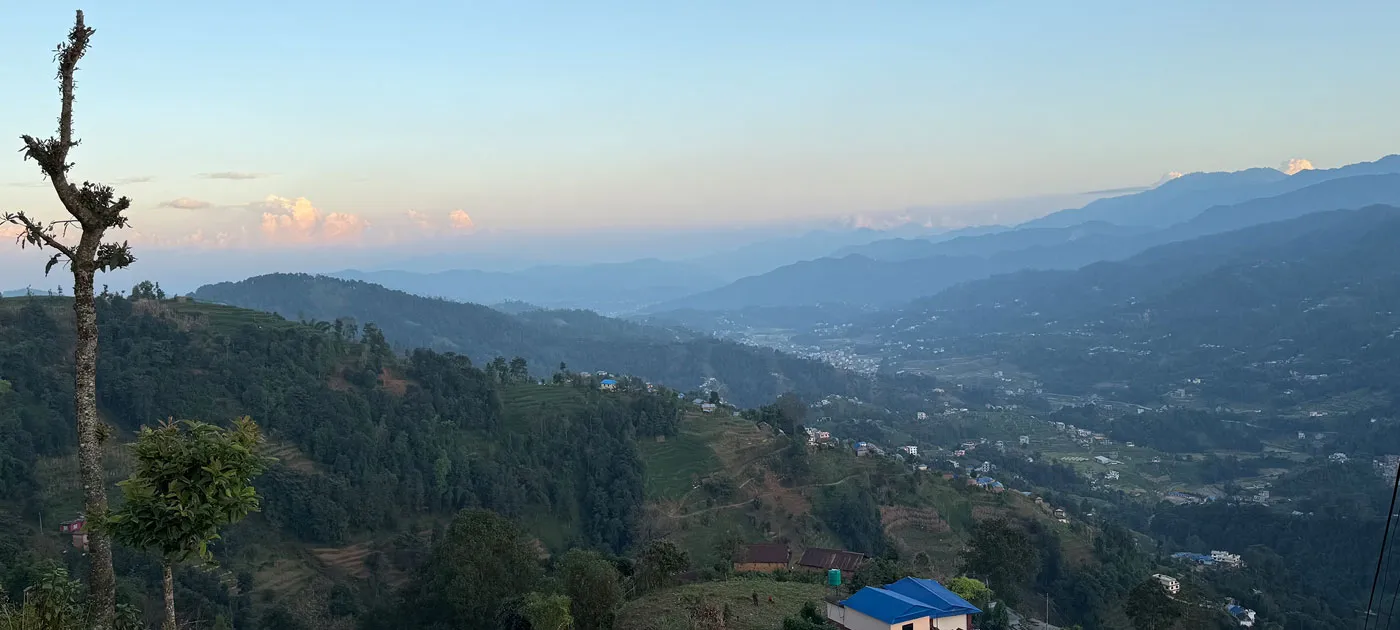 A wide scenic view over rolling green hills and a valley mist in Nepal under an overcast sky