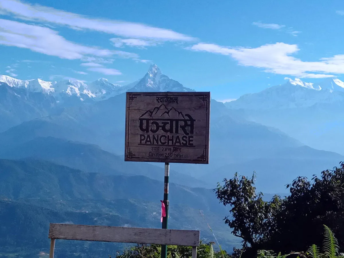 Wooden welcome signboard reading Panchase Elevation 2517 meters positioned in front of the snow-covered Annapurna Himalayan mountain range