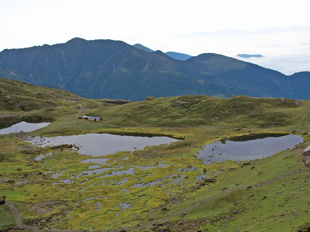 High-angle landscape view of the sacred Panch Pokhari glacial lakes surrounded by green meadows and distant misty mountains.