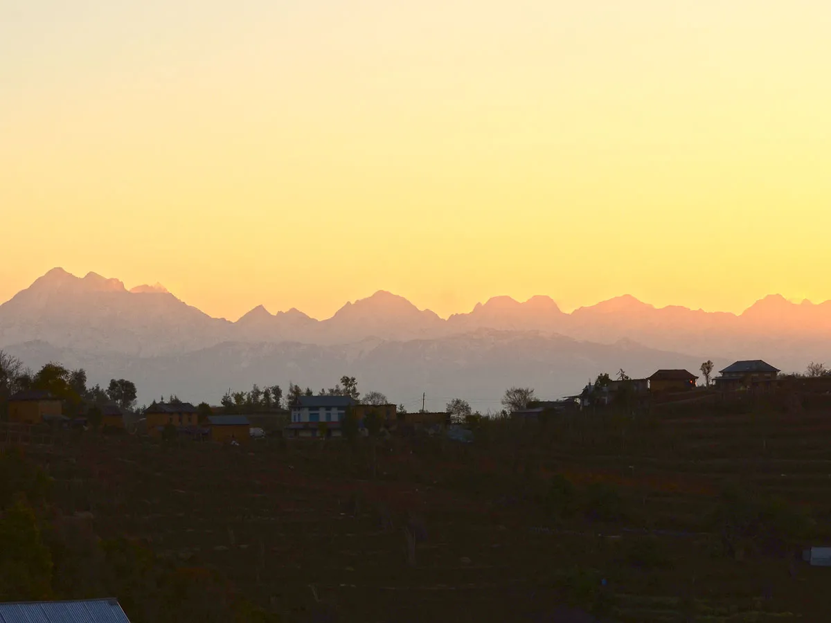 A dramatic mountain horizon showing snow-covered Himalayan peaks illuminated by the warm orange glow