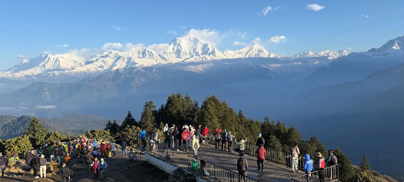A crowd of tourists gathered on the viewing platform at Poon Hill enjoying panoramic views of the snow-covered Annapurna mountain range.