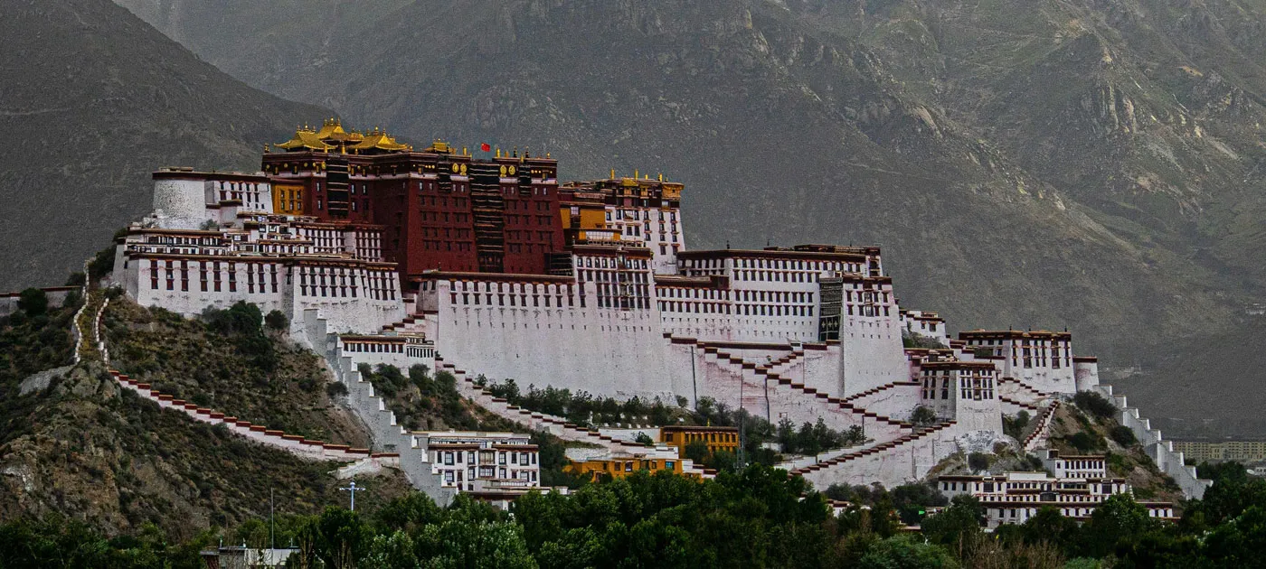 Panoramic view of the grand Potala Palace set against the rugged Himalayan mountain backdrop in Lhasa, Tibet.