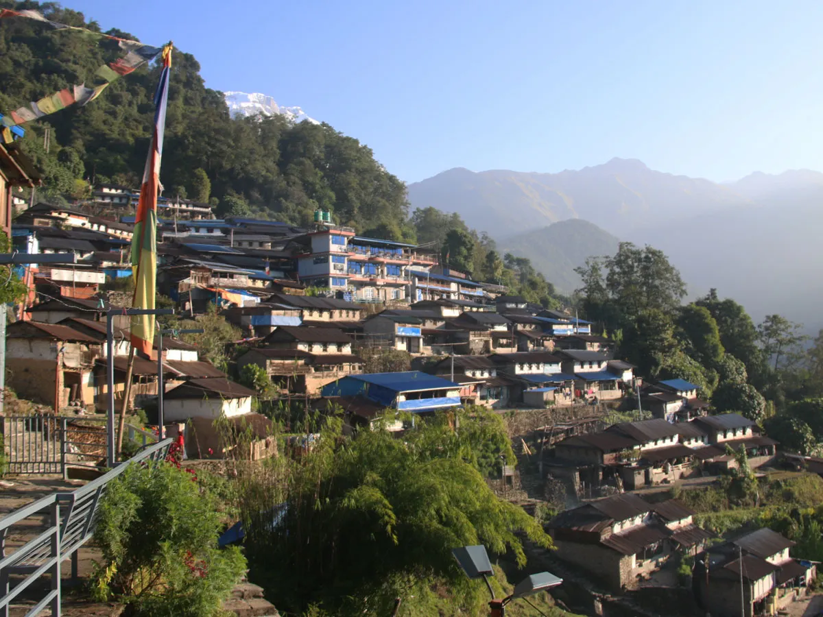 Traditional Gurung village of Sikles built on a hillside with prayer flags and mountains in the distance.