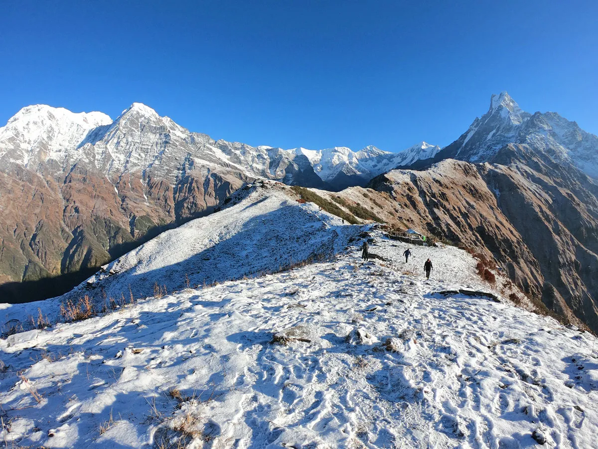 Trekkers walking along a snow-covered mountain ridge with snow-capped Himalayan peaks in the background