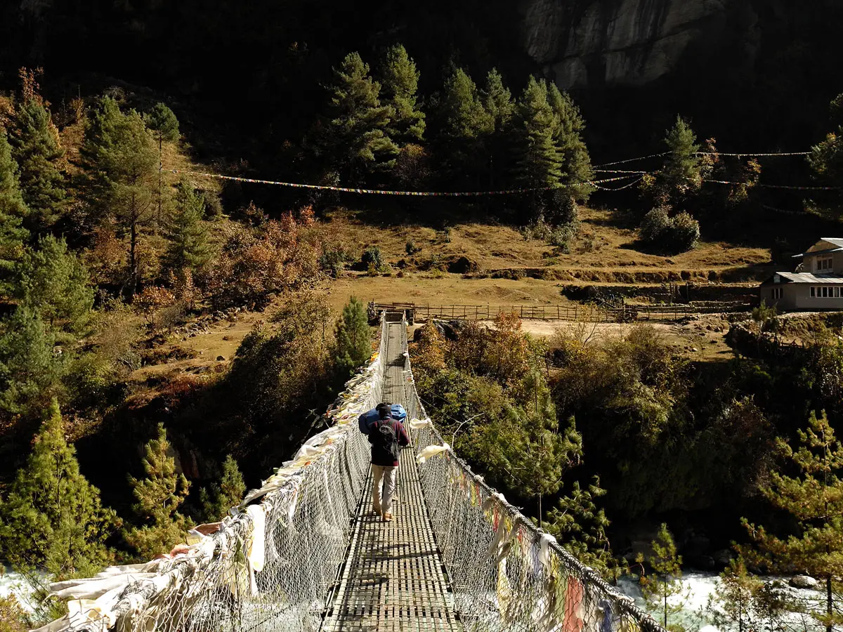 Trekker crossing a long suspension bridge adorned with prayer flags.