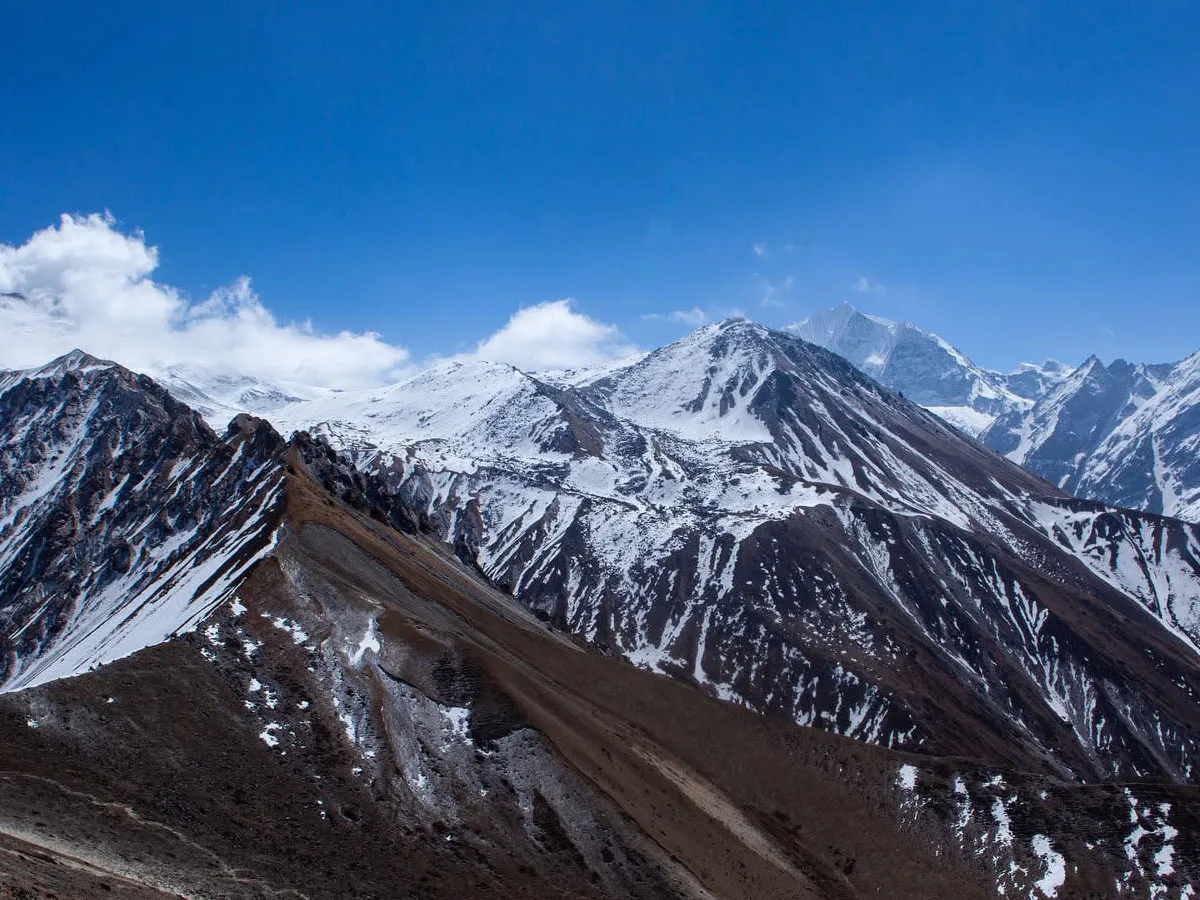 Panoramic view of snow-capped Himalayan mountain ridges and rugged high-altitude valleys under a clear blue sky in the Langtang region.