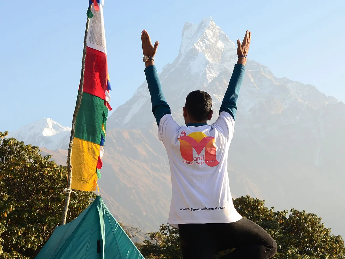 A yoga instructor facing away from the camera in a tree pose with raised arms, looking toward the iconic Machhapuchhre Fishtail peak in Nepal.