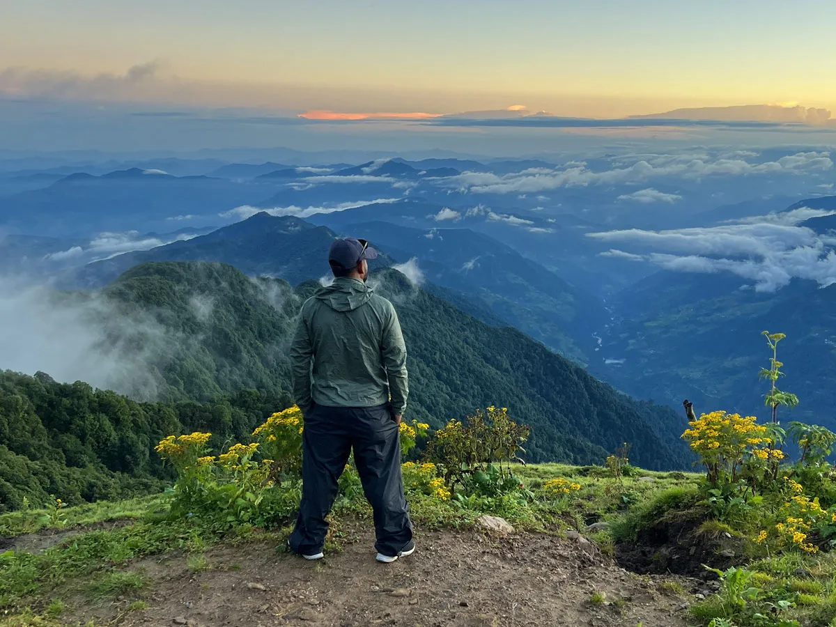 A hiker standing on a ridge looking out at misty green valleys and mountains during the Ghorepani Mardi Himal Trek