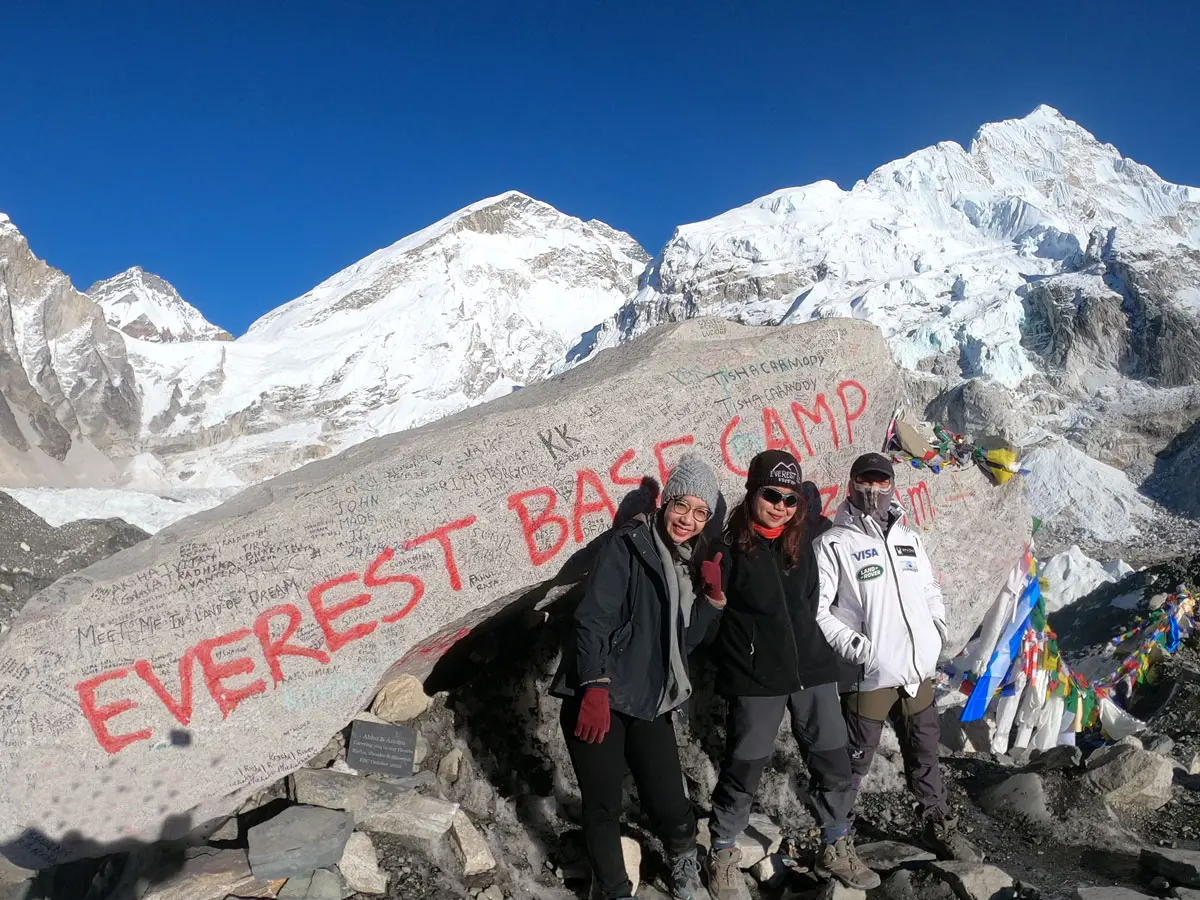 Three trekkers standing at the Everest Base Camp painted rock.