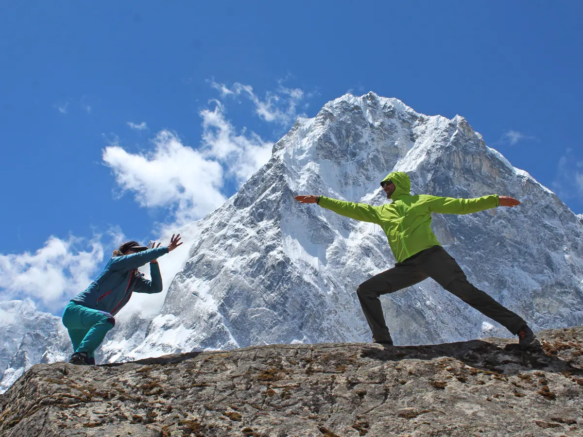 Trekkers posing playfully in Warrior II pose on a rocky trail with Mount Ama Dablam in the background