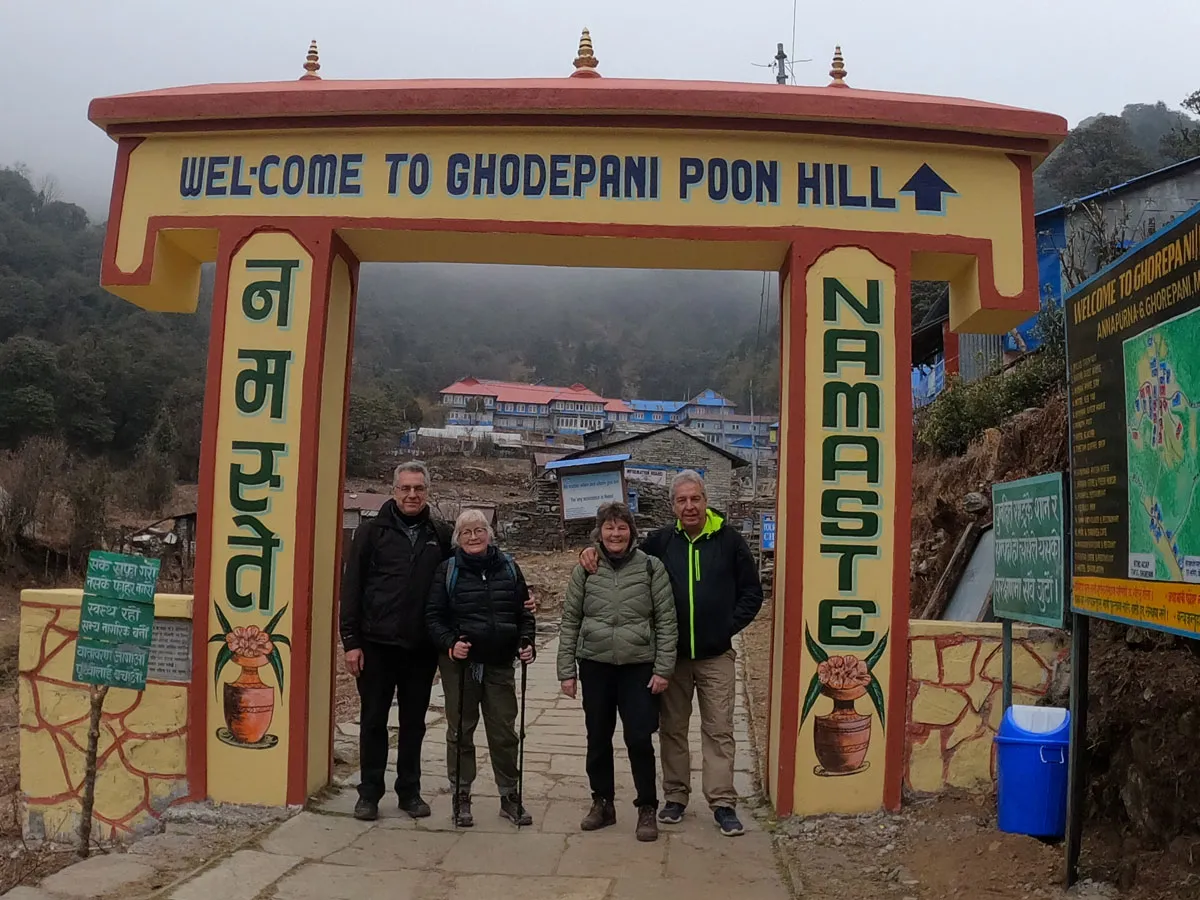 Group of hikers standing in front of the Welcome to Ghorepani Poon Hill archway in Nepal.