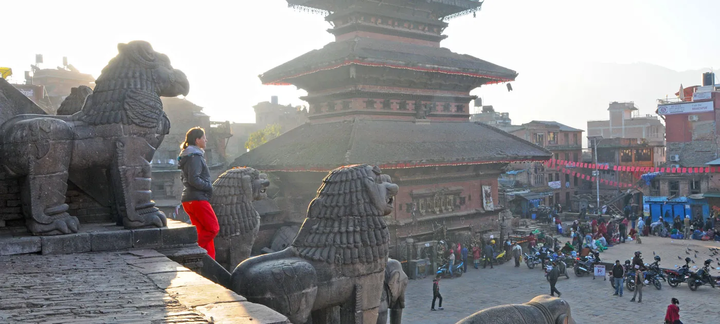 A traveler standing near ancient stone guardian lion statues at Bhaktapur Durbar Square facing a multi-tiered pagoda temple