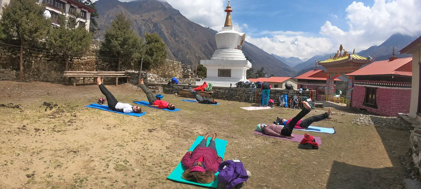 Group of practitioners on yoga mats practicing outdoors in front of a white Buddhist stupa and monastery in the Himalayas