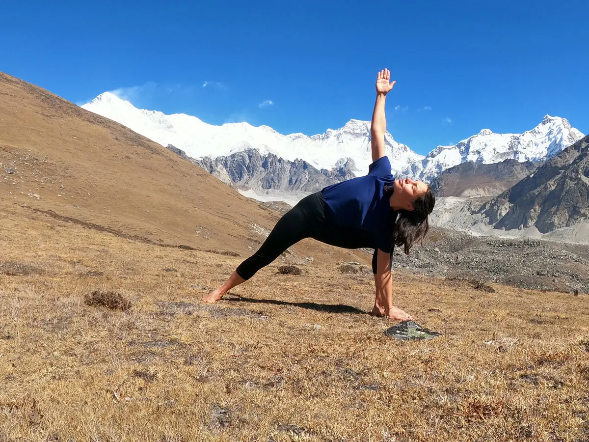 Woman practicing Extended Side Angle yoga pose in front of snow-capped Himalayan peaks
