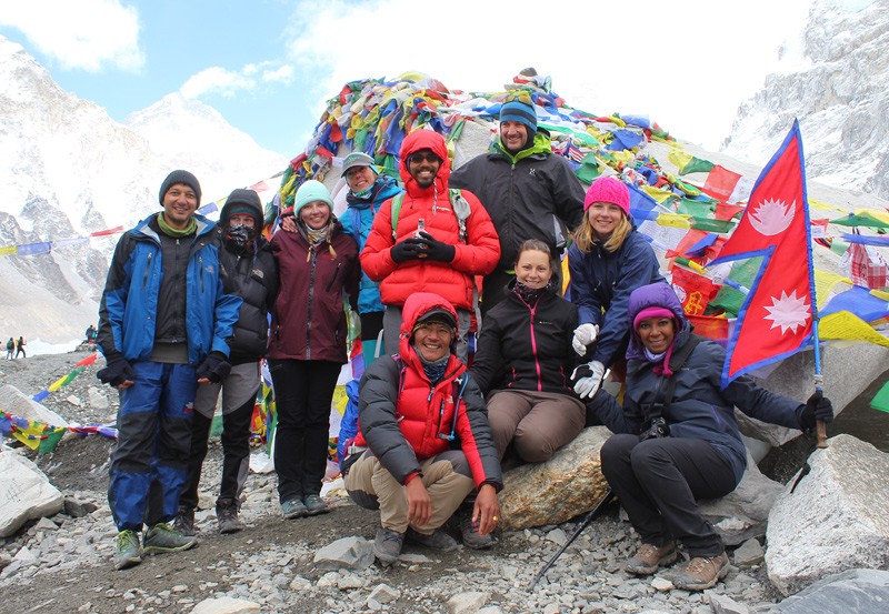 A smiling group of Rugged Trails Nepal trekkers at the landmark Everest Base Camp rock