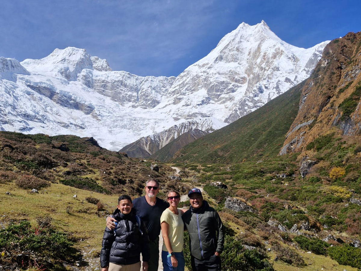 Happy trekking group and local guides smiling together against a backdrop of majestic, snow-capped Himalayan peaks on the Manaslu Circuit