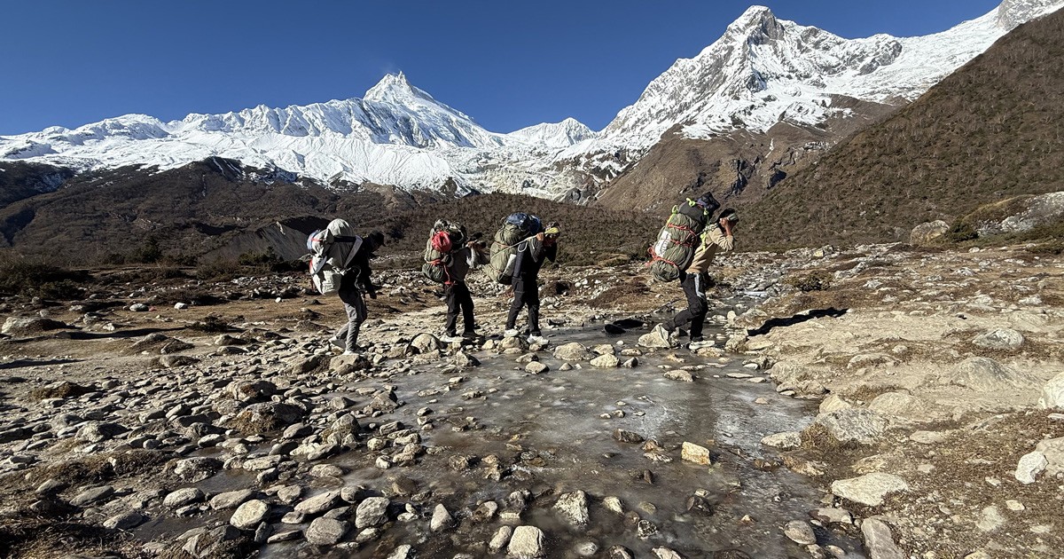 porters crossing the icy trail and manaslu on backdrop