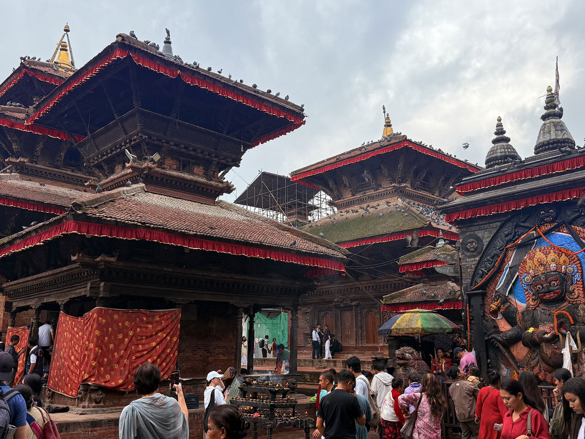 Crowd of visitors gathered near traditional pagoda-style temples and the large relief sculpture of Kal Bhairav in Kathmandu Durbar Square