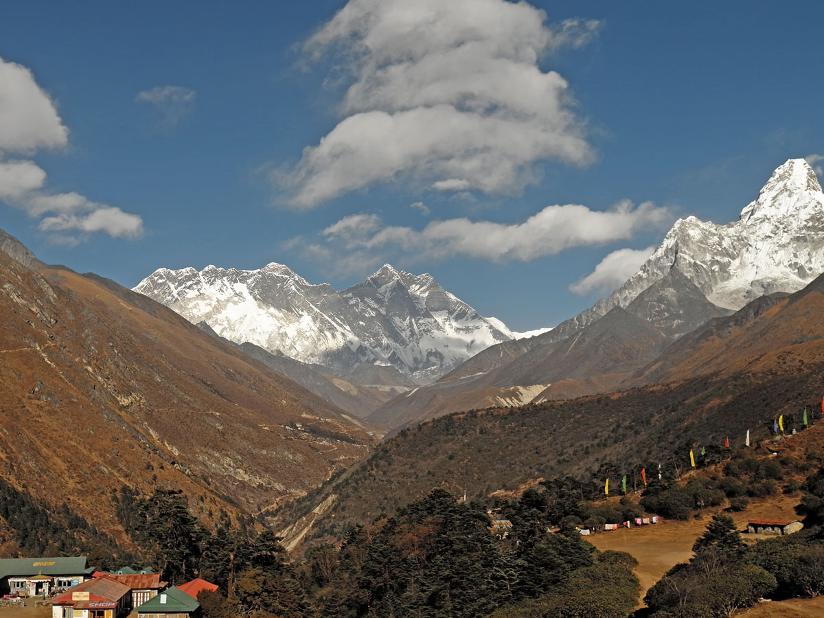 Panoramic view of Mount Everest, Lhotse, and Ama Dablam standing above forested valleys and alpine lodges