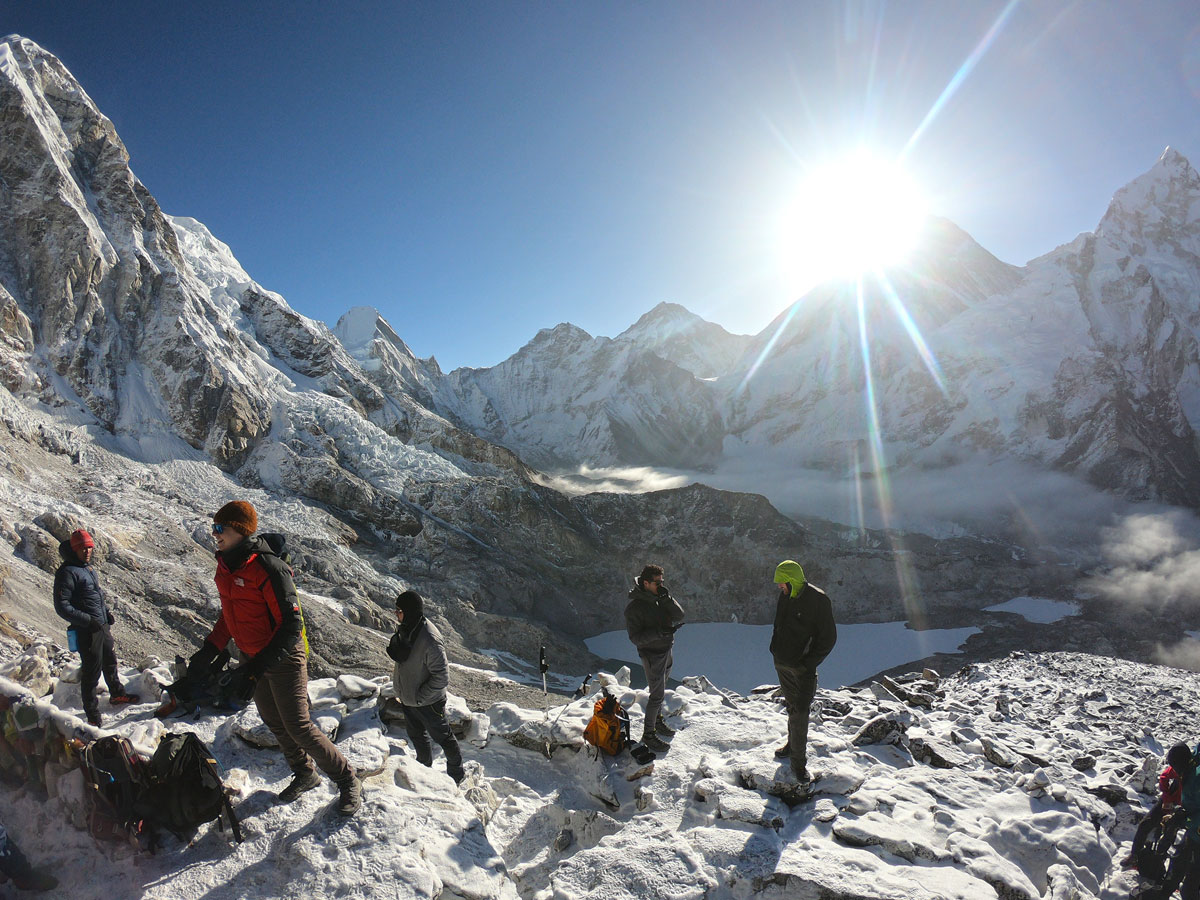 Trekkers on snow-covered Kala Patthar viewpoint with bright sunlight bursting behind snow-capped Himalayan peaks