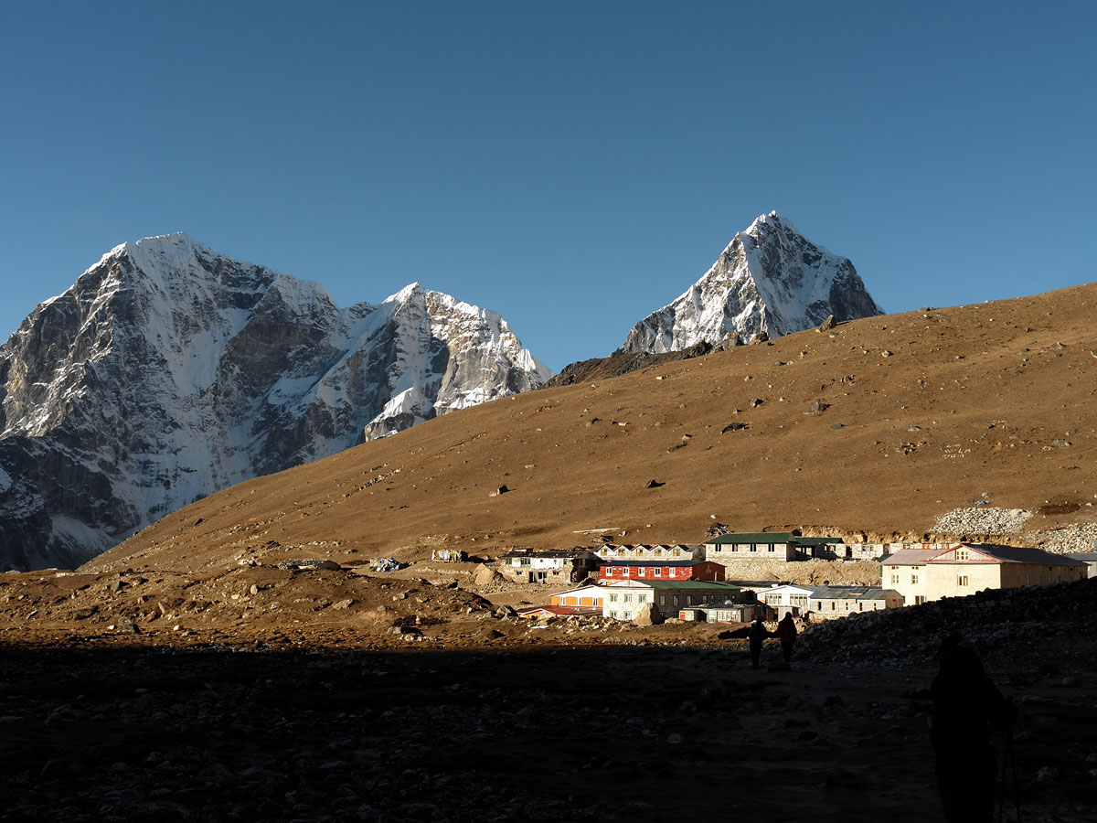 Small mountain settlement of Lobuche situated at the foot of brown alpine slopes with steep snow-covered peaks rising in the background