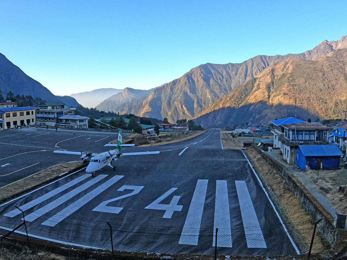 Small twin-otter aircraft parked on Runway 24 at Lukla Airport with steep mountain slopes in the background