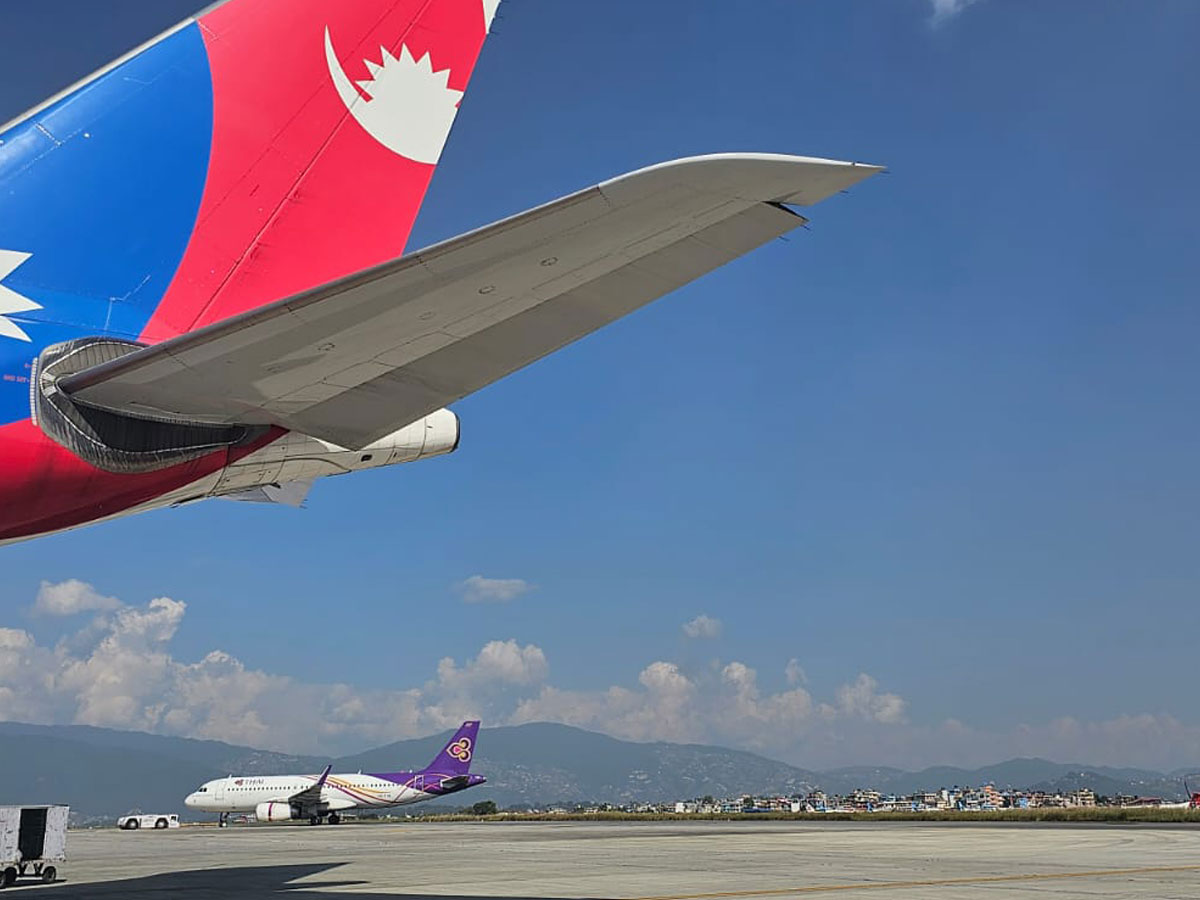 Tail fin of a Nepal Airlines aircraft bearing the flag of Nepal parked on the tarmac at Tribhuvan International Airport with mountains in the background