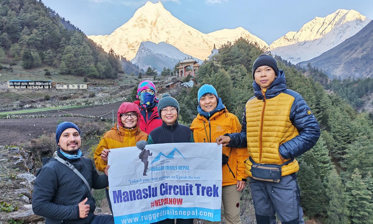 A group of five trekkers from Rugged Trails Nepal posing with a "Manaslu Circuit Trek" banner in Lho village