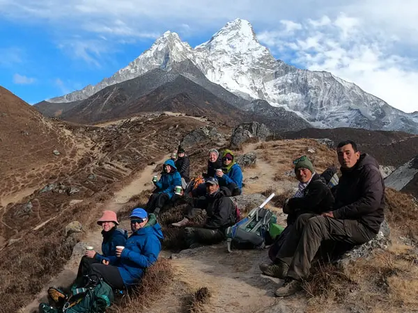 A group of trekkers resting on a trail with Mount Ama Dablam in the background.