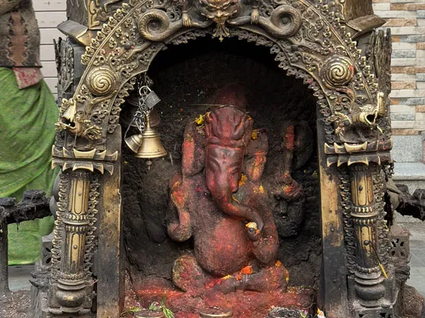 A small stone idol of Lord Ganesha coated in sacred red vermilion paste, housed inside an intricately carved brass shrine