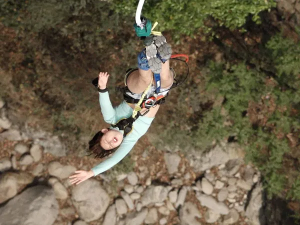 A thrill-seeker diving headfirst upside down during a bungee jump above a rocky river canyon