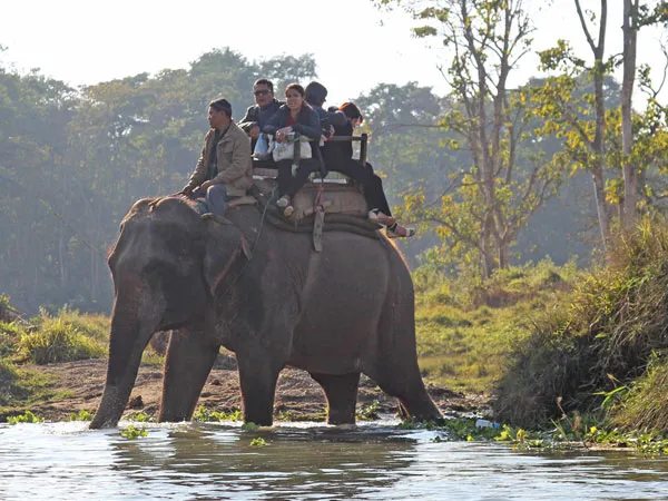 Tourists riding an elephant through a river crossing during a Chitwan National Park jungle safari in Nepal