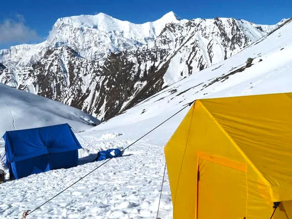 Yellow and blue mountaineering tents set up on a snow slope at High Camp, with giant snow-capped Himalayan peaks