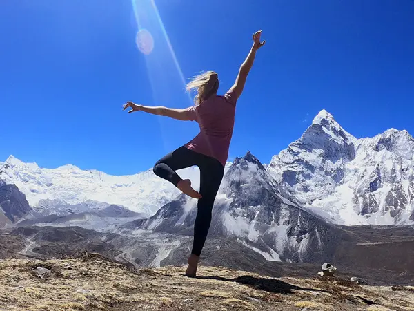 Trekker posing on the Everest Base Camp trail with snow-capped mountain peaks behind her