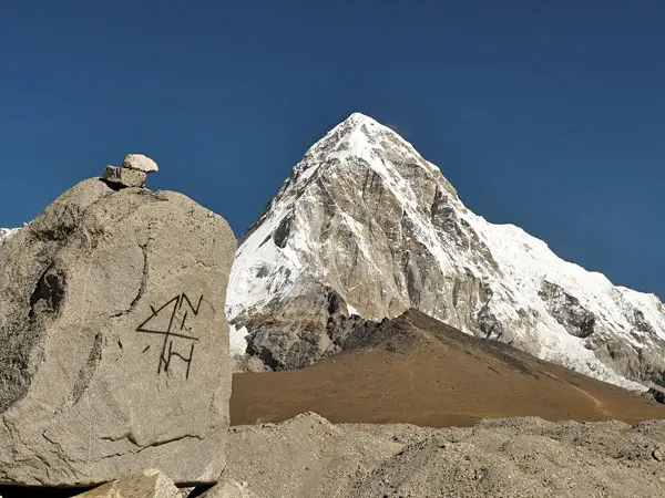 Marked boulder foreground with Mount Pumori's snow peak under blue sky on Everest trail