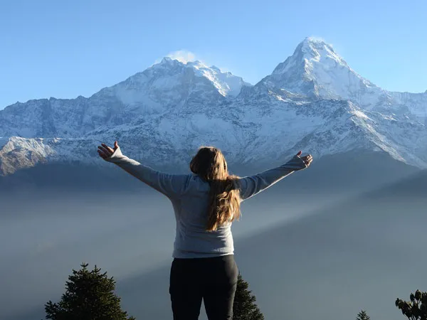 A female trekker standing with arms outstretched towards the snow-capped Annapurna mountain range during the Ghorepani Poon Hill and Mardi Himal trek in Nepal.