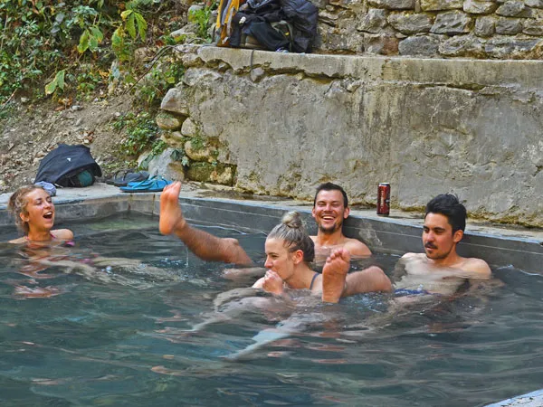 A group of happy trekkers relaxing and laughing in the natural hot spring pool at Jhinu Danda during the Ghorepani Poon Hill trek in Nepal.