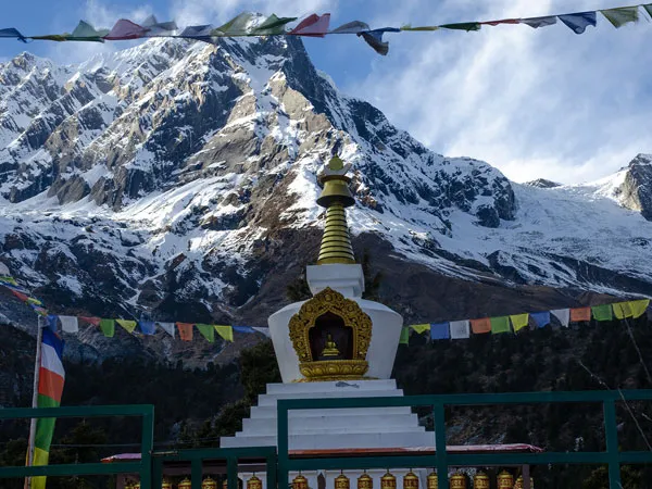 A Buddhist stupa and colorful prayer flags set against a dramatic backdrop of snow-covered Himalayan mountain peaks