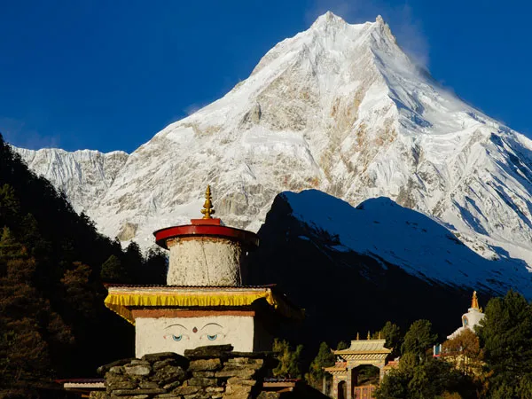 Traditional Buddhist stupa featuring Buddha eyes set against the towering, snow-capped peak of Mount Manaslu under a clear blue sky.